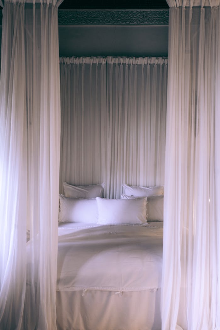 A cozy and serene canopy bed draped with translucent white curtains creating a tranquil bedroom setting.